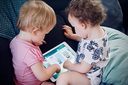 Two children interact with a tablet by tapping on the screen.
