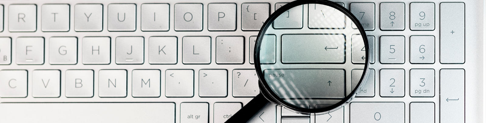 A magnifying glass resting on top of the enter key of a laptop.