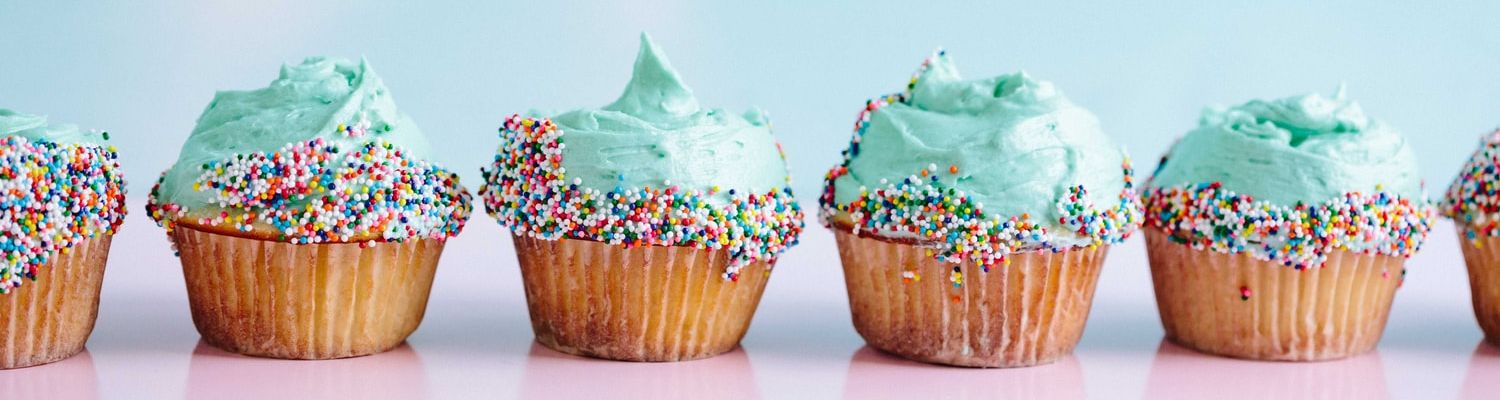 Baking and Cooking header: Line of blue-frosted cupcakes with rainbow nonpareil sprinkles