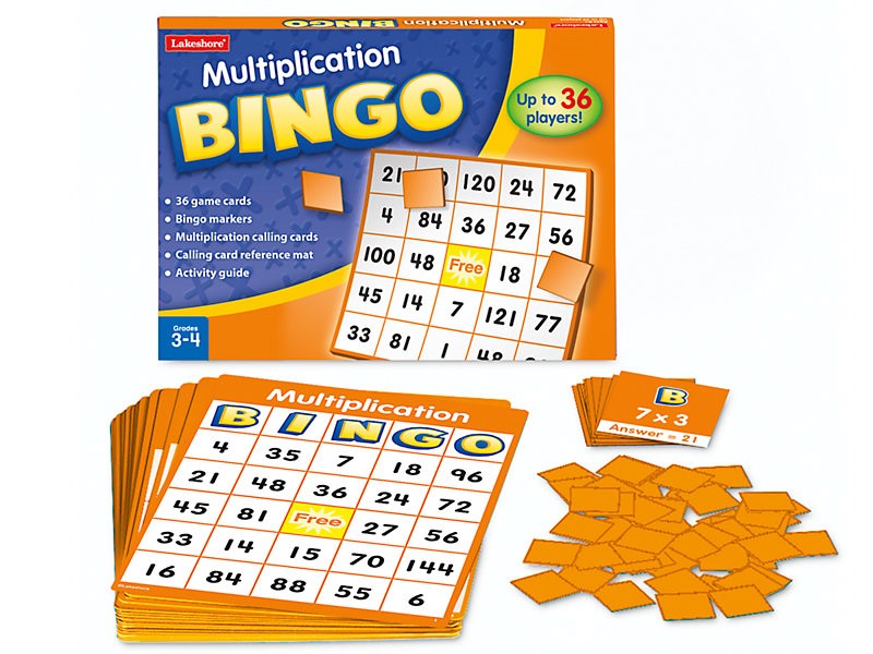 Box for Multiplication BINGO next to a pile of cardboard marking pieces, calling cards, and a BINGO card. The top BINGO card has 24 spaces, each with a different number. The top calling card reads 7 multiplied by 3, Answer equals 21.