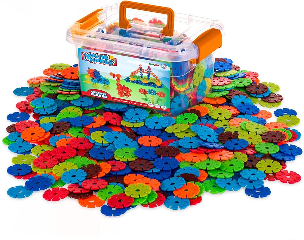 ID: Creative Flakes (interlocking plastic discs) in spread-out pile with plastic container sitting in top. Container houses more Creative Flakes.