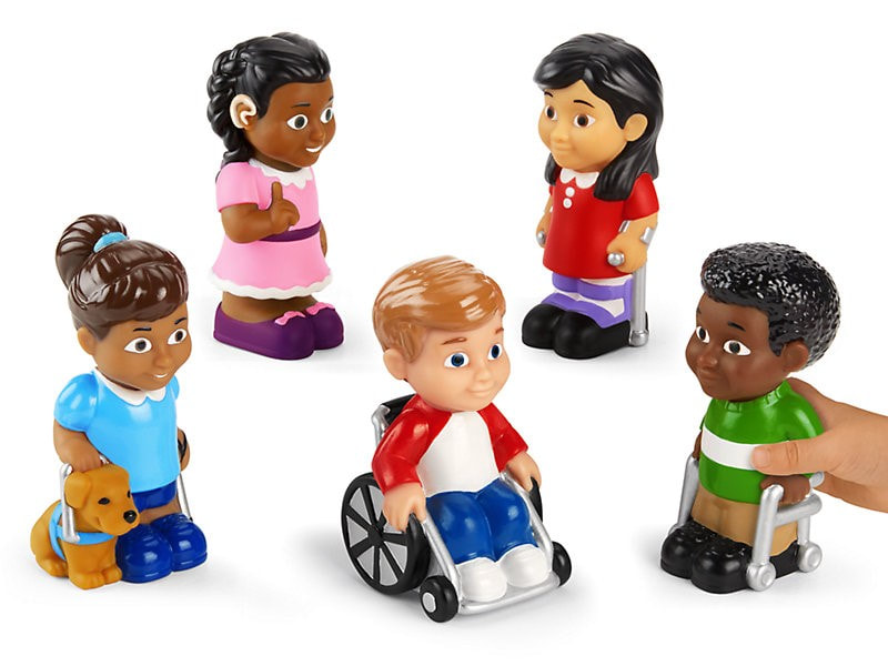 Five small dolls. From left to right the dolls are a bi-racially-coded girl with a guide dog, a Hispanic-coded girl with a hearing aide, a white--coded boy in a wheelchair, an Asian-coded girl on crutches, and a Black-coded boy with a walker.