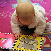 Baby looks down at a book with an elephant pictured.