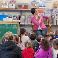 Adult sitting in front of a large group of children reading a story.